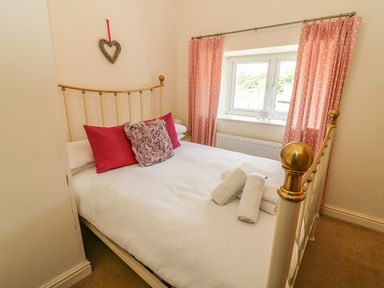 A bedroom with a brass bed frame pink pillows white towels on the bed and pink polka dot curtains at Woodbine Cottage in Ambleside