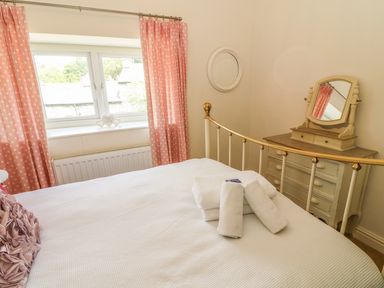 A bedroom with a bed, pink polka dot curtains, a chest of drawers with a mirror, and towels on the bed at Woodbine Cottage in Ambleside