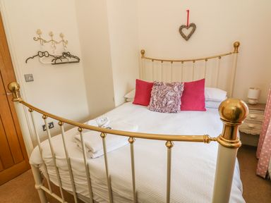 A bedroom with a metal bed frame with white bedding and pink cushions at Woodbine Cottage in Ambleside