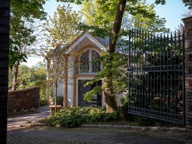 A gated entrance with iron gates and a driveway leading to a house surrounded by trees and shrubs at Hunters Moon in Charlestown