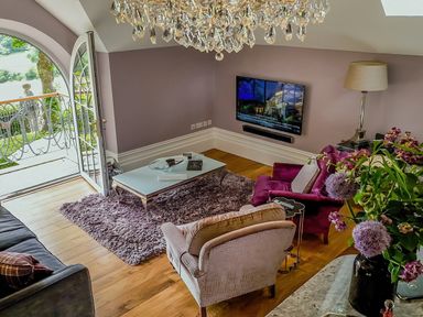 A living room with a chandelier wooden floor a rug and a glass door leading outside at Hunters Moon in Charlestown