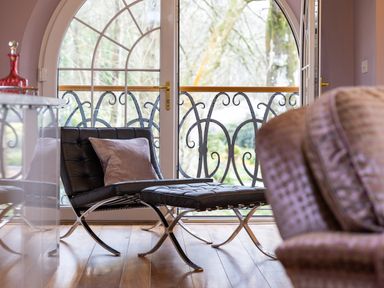A room with a black leather chair and ottoman near arched glass doors with a decorative metal balcony at Hunters Moon in Charlestown