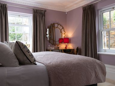 A bedroom with a bed near two windows and a dresser with a lamp and mirror at Hunters Moon in Charlestown