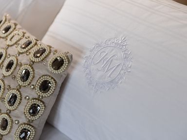 A decorative pillow with beads and gemstones on a white bed sheet with embroidered initials JM at Hunters Moon in Charlestown
