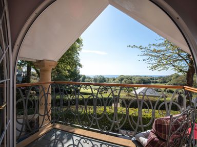 A balcony with an ornate metal railing and a chair overlooking trees and fields at Hunters Moon in Charlestown