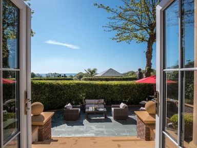 An outdoor patio with wicker furniture and a red umbrella viewed through open double doors at Hunters Moon in Charlestown