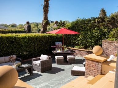 An outdoor patio with wicker furniture a red umbrella and a barbecue grill at Hunters Moon in Charlestown