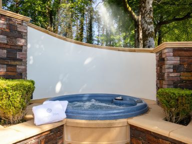 An outdoor hot tub with water jets surrounded by stone walls and green bushes at Hunters Moon in Charlestown
