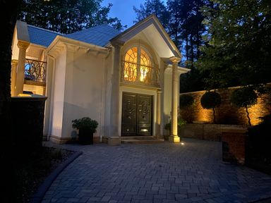 Exterior of a house with columns and large double doors lit at dusk with a paved driveway and trimmed trees at Hunters Moon in Charlestown