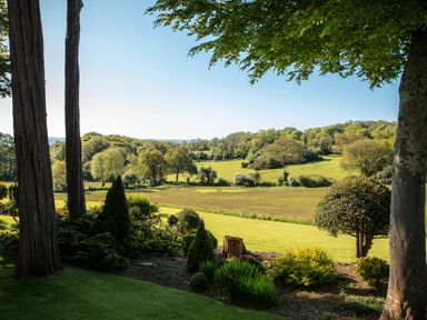 A garden with trees shrubs and grass overlooking fields and woodland at Hunters Moon in Charlestown