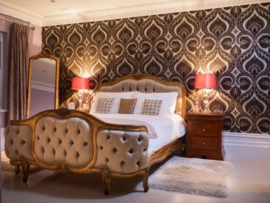 A bedroom with an upholstered bed wooden nightstands with lamps and a full length mirror at Hunters Moon in Charlestown