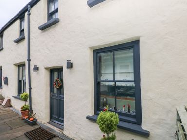 The exterior of a cream cottage with dark framed windows and door with a wreath at Blacksmiths Cottage in Pembroke