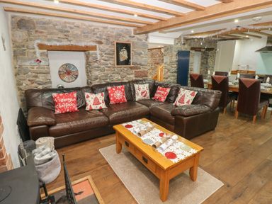 A living room with a leather sofa and Christmas cushions a wooden coffee table and a stone wall at Blacksmiths Cottage in Pembroke