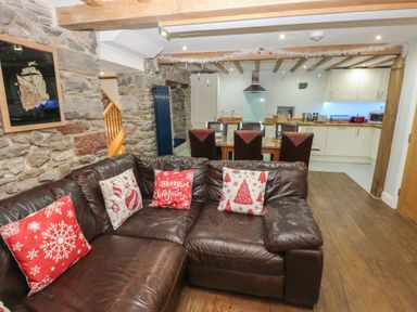 A living room with a brown leather sofa with Christmas cushions next to a kitchen and dining area with chairs at Blacksmiths Cottage in Pembroke