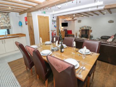 A dining area with a wooden table set for six and a kitchen area with white cabinets at Blacksmiths Cottage in Pembroke