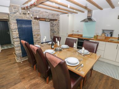 A dining table set for six in a kitchen with wooden beams and stone walls at Blacksmiths Cottage in Pembroke