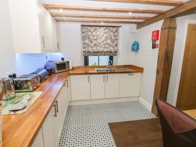 A kitchen with wooden countertops white cabinets a patterned window blind and various appliances at Blacksmiths Cottage in Pembroke