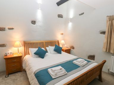 A bedroom with a wooden bed frame bedside tables lamps and folded towels at Blacksmiths Cottage in Pembroke