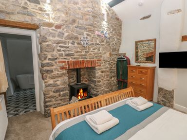 A bedroom with a wooden bed a stone fireplace with wood stove a wooden dresser and a wall-mounted TV at Blacksmiths Cottage in Pembroke