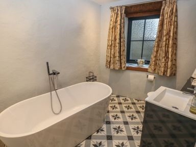 A bathroom with a freestanding bathtub patterned floor tiles a window with curtains and a sink at Blacksmiths Cottage in Pembroke