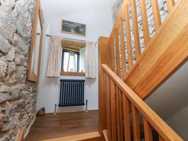 A stairway landing with wooden railing a window with curtains a dark radiator and stone walls at Blacksmiths Cottage in Pembroke