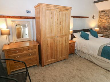 A bedroom with a wooden wardrobe chest of drawers a bed with pillows and bedside tables with lamps at Blacksmiths Cottage in Pembroke
