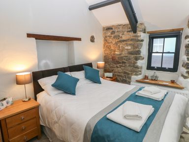 A bedroom with a double bed with blue pillows and folded towels on a runner two bedside tables with lamps and a window at Blacksmiths Cottage in Pembroke