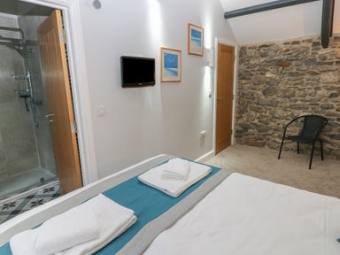 A bedroom with a bed and towels next to a stone wall and a door leading to a bathroom at Blacksmiths Cottage in Pembroke