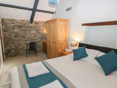 A bedroom with a double bed blue pillows wooden wardrobe black chair and stone wall at Blacksmiths Cottage in Pembroke