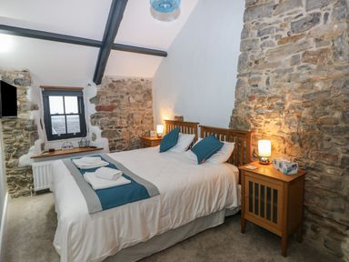 A bedroom with a double bed between two wooden nightstands and exposed stone walls at Blacksmiths Cottage in Pembroke