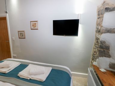 A bedroom with a bed with folded towels a wall mounted television and stone fireplace at Blacksmiths Cottage in Pembroke