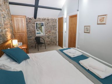 A bedroom with a bed and pillows a wooden wardrobe a chair a mirror and two wooden doors at Blacksmiths Cottage in Pembroke
