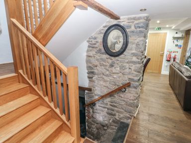 A wooden staircase with a stone wall and framed picture in a hallway with leather sofas at Blacksmiths Cottage in Pembroke