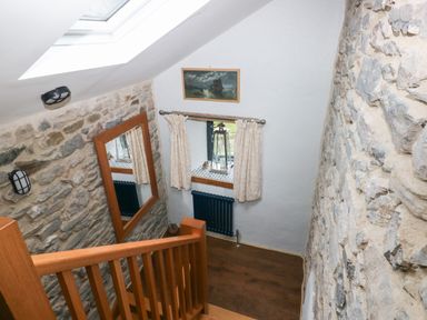 A stairway with wooden railing and stone walls with a mirror and a window at Blacksmiths Cottage in Pembroke