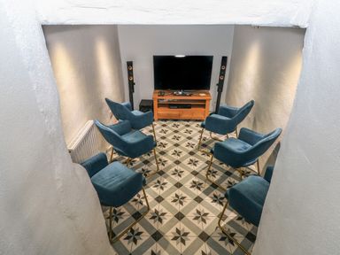 A small room with six blue chairs facing a television on a wooden stand at Blacksmiths Cottage in Pembroke