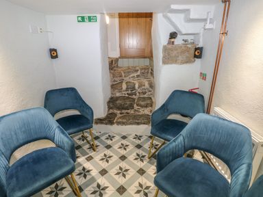 A small room with four blue chairs arranged on patterned floor tiles and stone steps leading to a wooden door at Blacksmiths Cottage in Pembroke