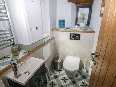 A small bathroom with a toilet a sink a boiler and patterned floor tiles at Blacksmiths Cottage in Pembroke