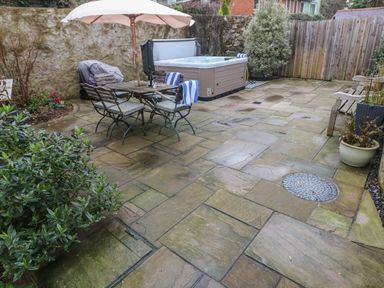 A patio with outdoor dining table and chairs under an umbrella hot tub and plants at Blacksmiths Cottage in Pembroke