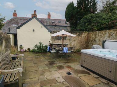 An outdoor patio with a hot tub wooden bench table with umbrella chairs and stone walls at Blacksmiths Cottage in Pembroke