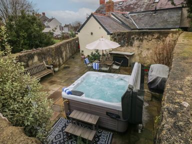 An outdoor patio area with a hot tub towels wooden bench table with umbrella and chairs at Blacksmiths Cottage in Pembroke
