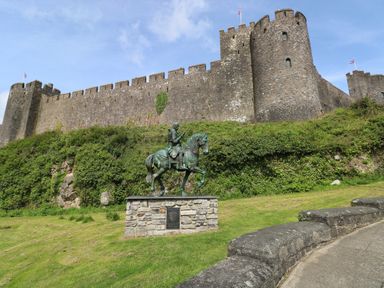 A statue of a man on horseback in front of a stone castle with battlements and grassy area at Blacksmiths Cottage in Pembroke