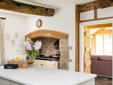 A kitchen with flowers on a counter and an open doorway to a living area at Henhouse Farm Bodenham