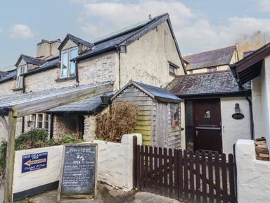 Exterior view of a stone and plaster building with a wooden gate and signs for The Grampus Inn and Old Farm Cottage in Woolacombe