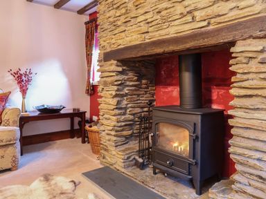 A room with a stone fireplace wood burning stove and a wooden table with a vase and a bowl at Old Farm Cottage in Woolacombe