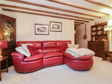 A living room with a red leather sectional sofa and framed pictures on the wall at Old Farm Cottage in Woolacombe