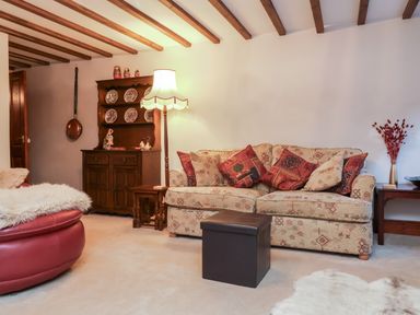 A living room with a patterned sofa and red pillows a wooden cabinet with plates and dolls a floor lamp and a round red chair at Old Farm Cottage in Woolacombe