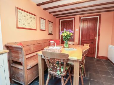 A dining area with a wooden table and chairs a wooden bench with cushions and flowers in a vase at Old Farm Cottage in Woolacombe