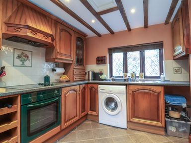 A kitchen with wooden cabinets a washing machine an oven and a window above the sink at Old Farm Cottage in Woolacombe