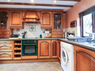 A kitchen with wooden cabinets a green oven a washing machine and a window at Old Farm Cottage in Woolacombe