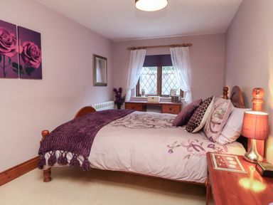 A bedroom with a wooden bed a bedside table with a lamp a wooden desk under a window with white curtains at Old Farm Cottage Woolacombe